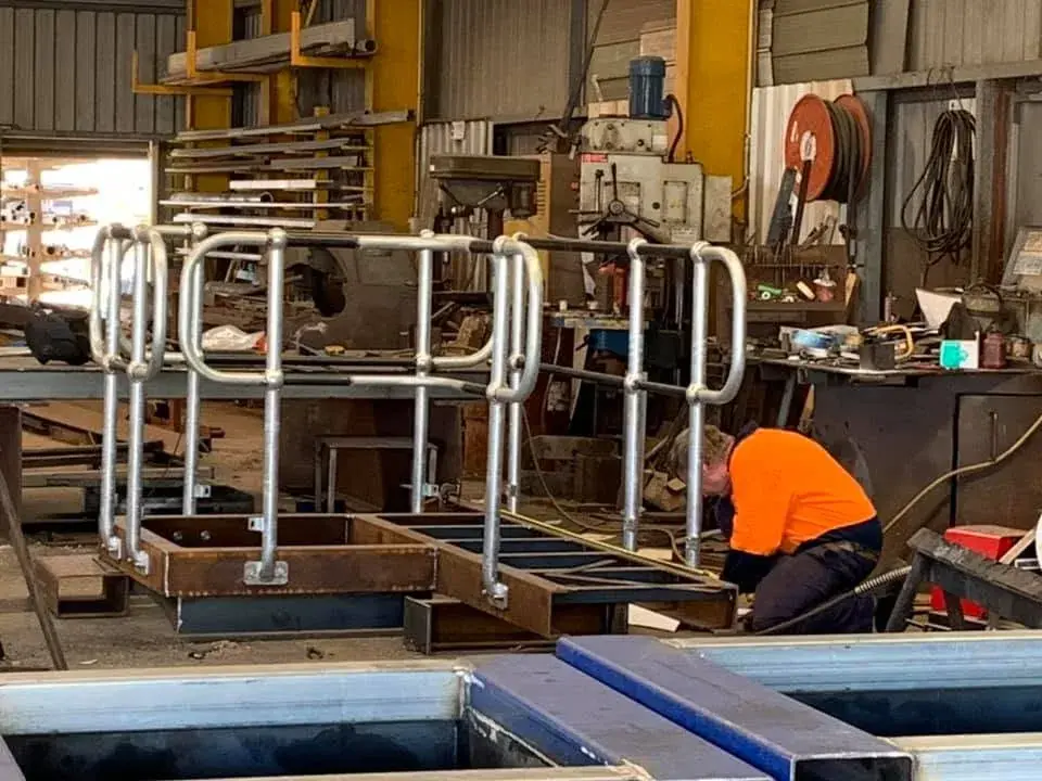 Welder in high-visibility clothing working on fabricated steel handrail frames in the workshop